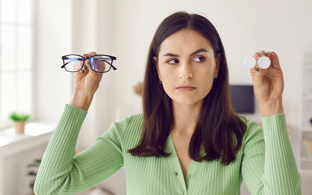 Frau hält eine Brille in der einen Hand und Kontaktlinsen in der anderen